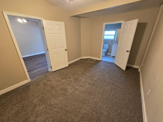 unfurnished bedroom featuring vaulted ceiling, dark carpet, and ensuite bathroom