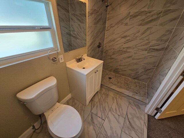 bathroom with toilet, tiled shower, and vanity