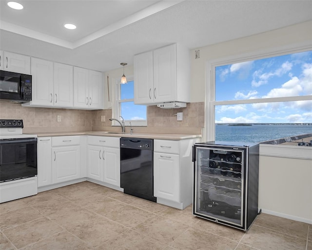 kitchen with tasteful backsplash, beverage cooler, white cabinets, black appliances, and a water view