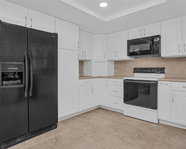 kitchen with decorative backsplash, black appliances, white cabinets, light tile patterned floors, and a tray ceiling