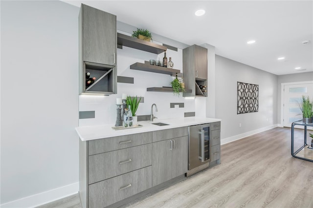 kitchen featuring gray cabinetry, beverage cooler, a sink, light wood-style floors, and open shelves