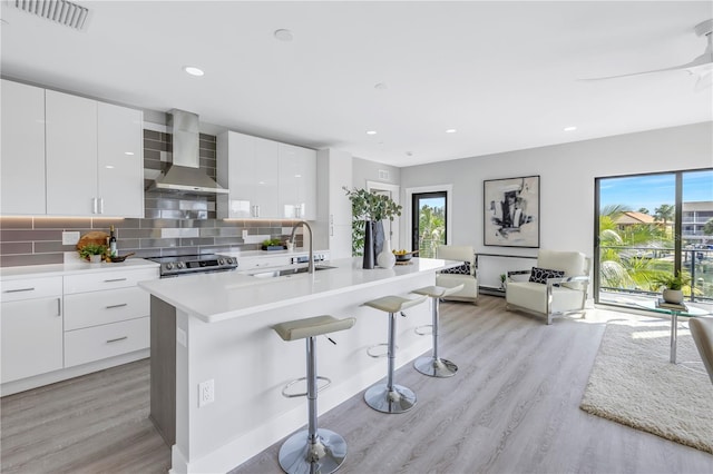 kitchen featuring white cabinets, light hardwood / wood-style flooring, wall chimney exhaust hood, a breakfast bar area, and decorative backsplash