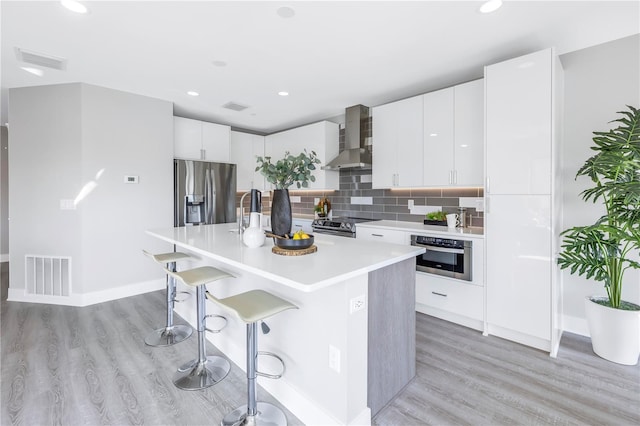 kitchen with light wood-type flooring, wall chimney exhaust hood, visible vents, and stainless steel appliances