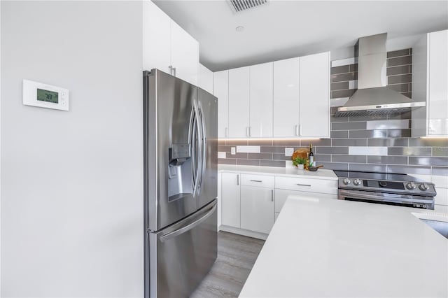 kitchen featuring stainless steel appliances, white cabinets, light countertops, decorative backsplash, and wall chimney exhaust hood