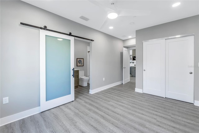 unfurnished bedroom featuring baseboards, a barn door, visible vents, and wood finished floors