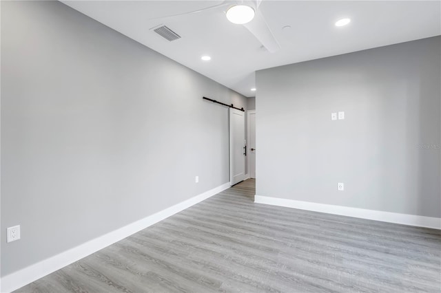 unfurnished room with a barn door, visible vents, baseboards, ceiling fan, and wood finished floors