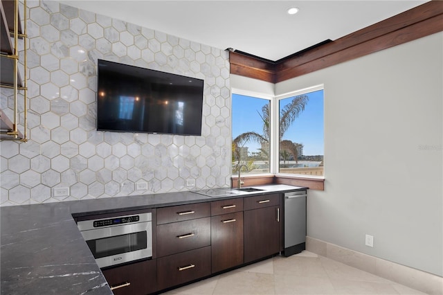 kitchen featuring light tile patterned floors, dark countertops, appliances with stainless steel finishes, a sink, and dark brown cabinets