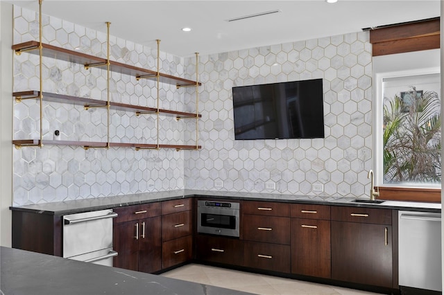 kitchen featuring dark countertops, a sink, stainless steel appliances, backsplash, and light tile patterned flooring