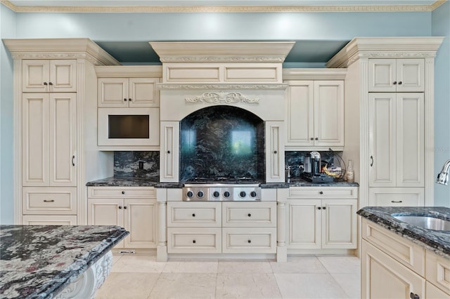 kitchen with tasteful backsplash, dark stone countertops, cream cabinetry, stainless steel gas cooktop, and a sink