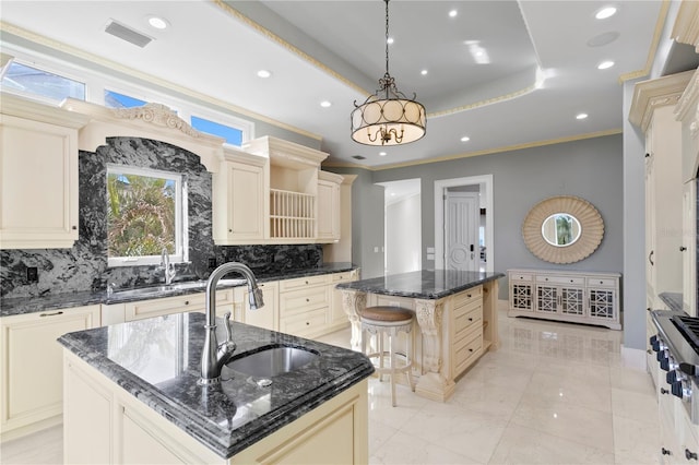 kitchen with a raised ceiling, cream cabinetry, an island with sink, and a sink