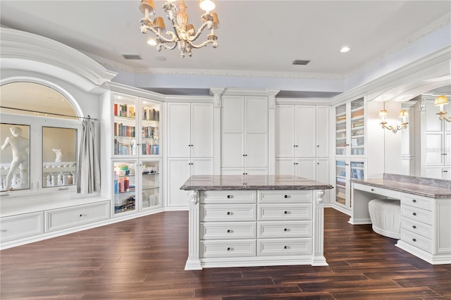 spacious closet with dark wood-style floors, visible vents, arched walkways, and an inviting chandelier