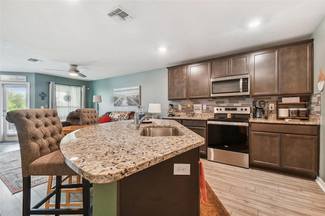 kitchen featuring appliances with stainless steel finishes, light hardwood / wood-style flooring, dark brown cabinetry, light stone counters, and sink