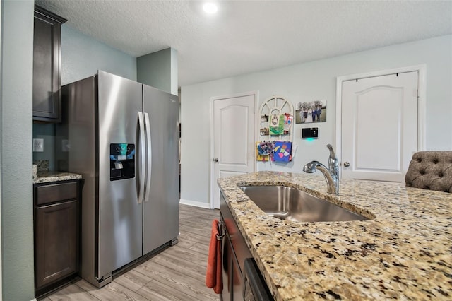 kitchen featuring light stone counters, a textured ceiling, stainless steel refrigerator with ice dispenser, sink, and light wood-type flooring