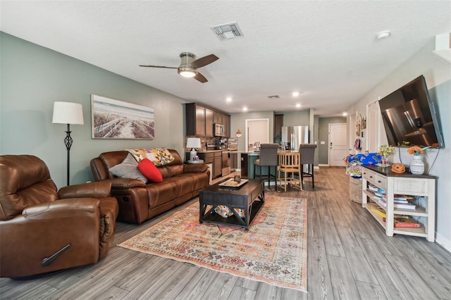 living room with ceiling fan, a textured ceiling, and light hardwood / wood-style flooring