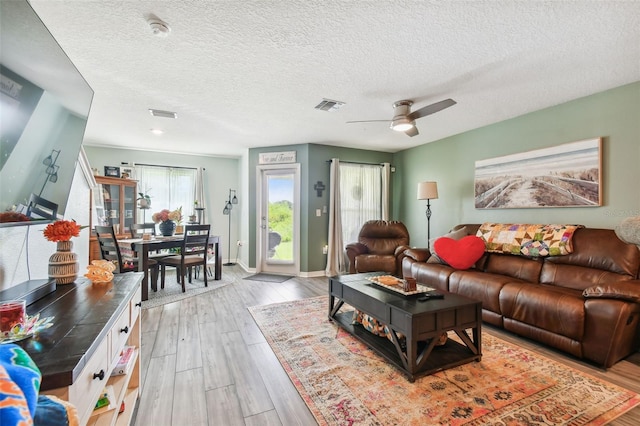 living room featuring light hardwood / wood-style floors, ceiling fan, and a textured ceiling