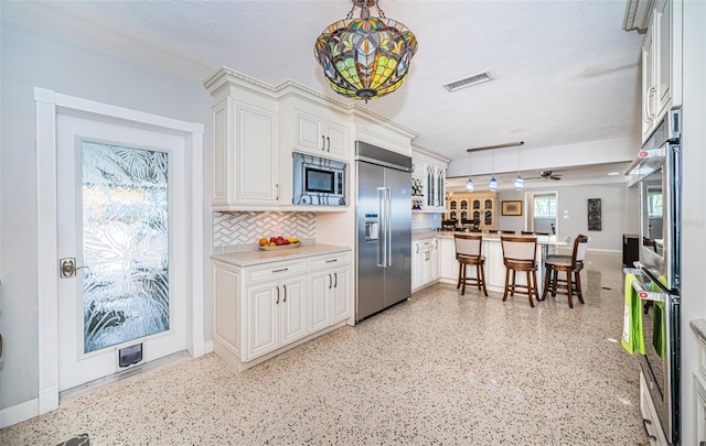 kitchen with built in appliances, a textured ceiling, white cabinets, decorative backsplash, and pendant lighting