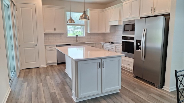 kitchen with a center island, light countertops, custom range hood, stainless steel appliances, and a sink