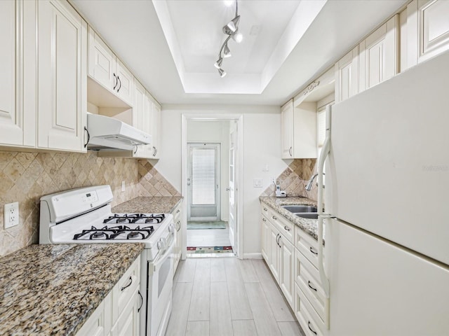 kitchen with white appliances, tasteful backsplash, a raised ceiling, under cabinet range hood, and a sink