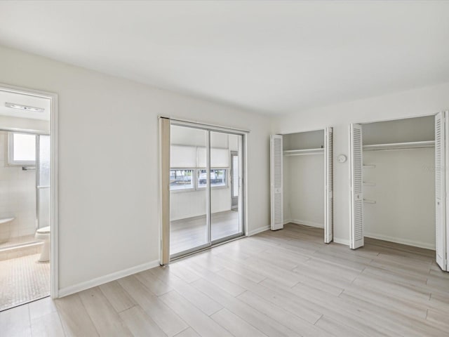 unfurnished bedroom with ensuite bath, light wood-type flooring, two closets, and baseboards