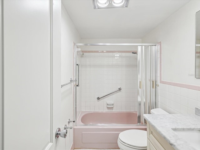 bathroom featuring wainscoting, toilet,  shower combination, vanity, and tile walls