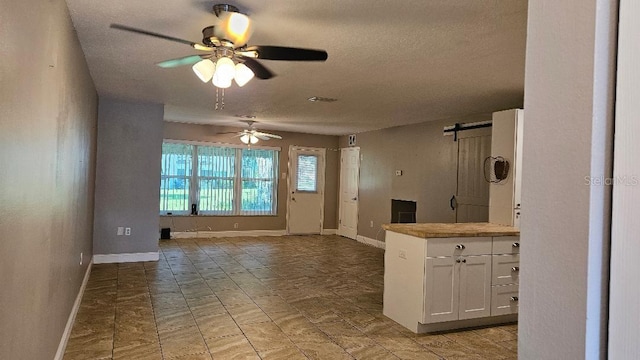 kitchen with ceiling fan, a barn door, white cabinets, light tile patterned floors, and a textured ceiling