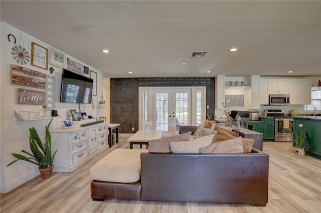 living room with french doors, a textured ceiling, light wood-type flooring, and a healthy amount of sunlight