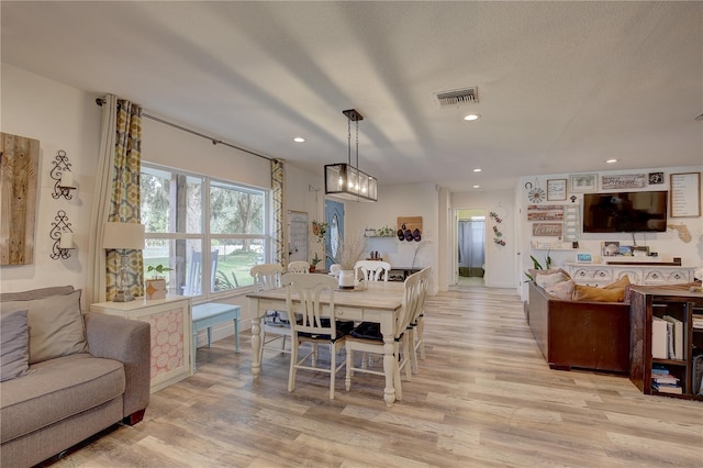 dining room with a textured ceiling, light hardwood / wood-style floors, and a notable chandelier