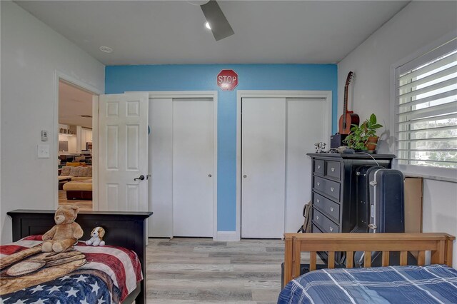 bedroom with light hardwood / wood-style floors, ceiling fan, and multiple closets