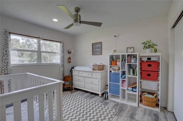 bedroom with ceiling fan, a crib, and hardwood / wood-style floors