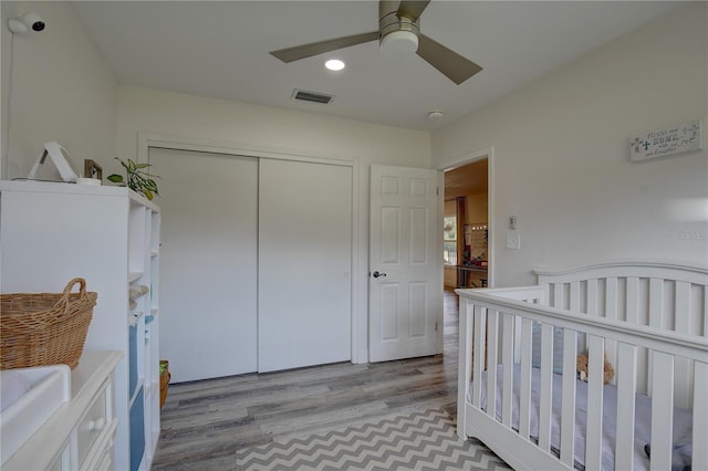 bedroom featuring a crib, light hardwood / wood-style flooring, a closet, and ceiling fan