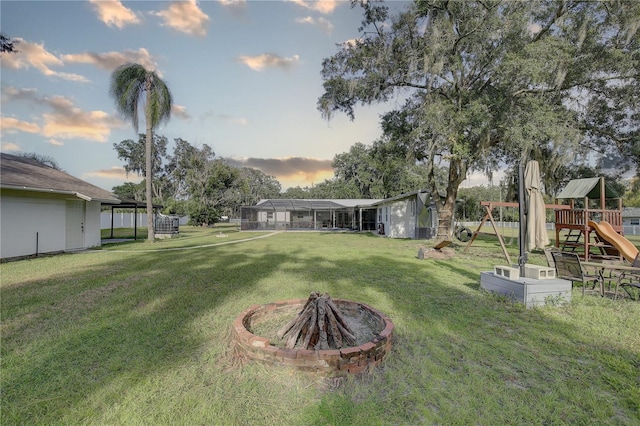 yard at dusk with a playground, a lanai, and a fire pit