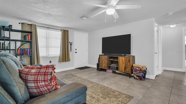 living room featuring light tile patterned floors, visible vents, ceiling fan, a textured ceiling, and baseboards