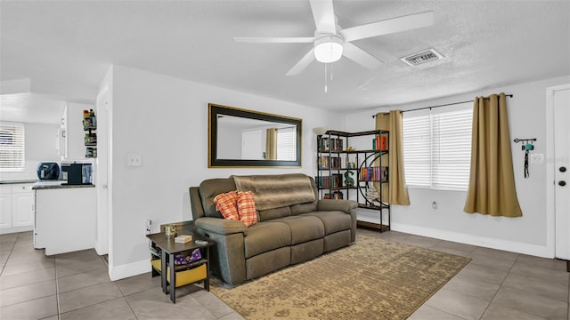 living area featuring baseboards, visible vents, a ceiling fan, tile patterned flooring, and a textured ceiling
