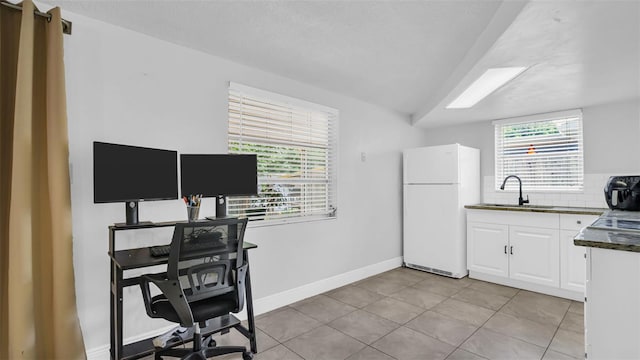 kitchen featuring a sink, white cabinets, a wealth of natural light, freestanding refrigerator, and dark countertops
