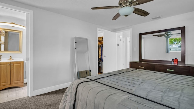 bedroom with light colored carpet, visible vents, a spacious closet, ensuite bathroom, and baseboards