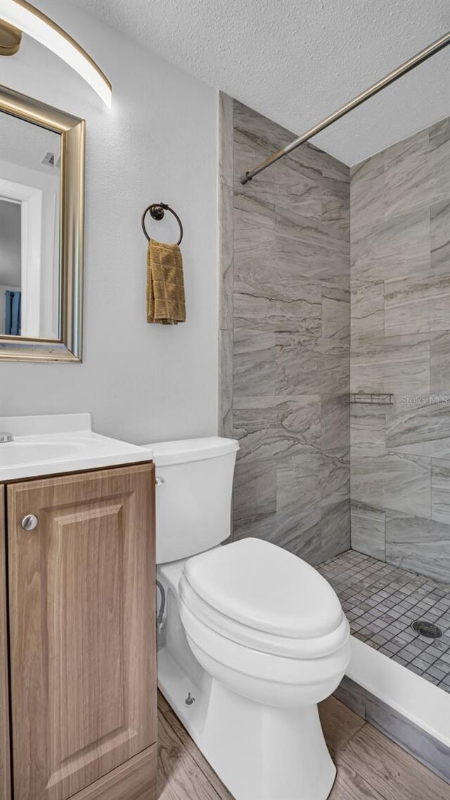 bathroom with vanity, a textured ceiling, a tile shower, wood-type flooring, and toilet