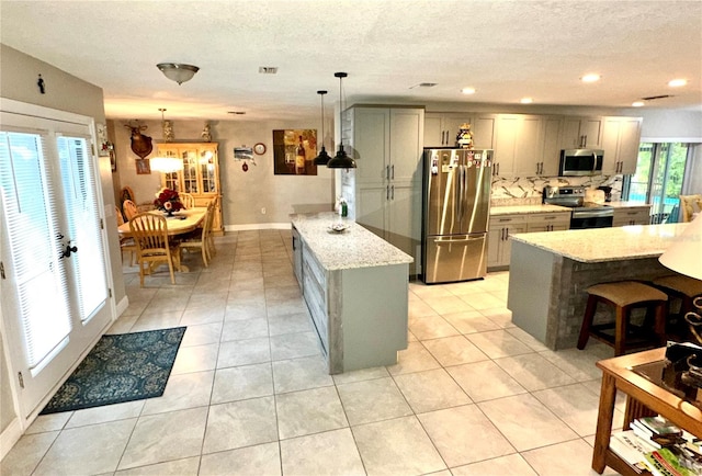 kitchen with gray cabinetry, hanging light fixtures, light tile patterned floors, appliances with stainless steel finishes, and light stone counters