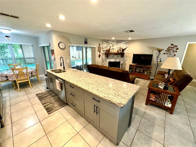 kitchen featuring dishwasher, sink, light stone counters, gray cabinets, and a center island with sink