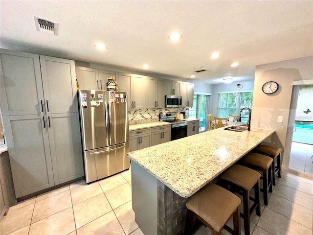 kitchen with light stone counters, sink, a kitchen island with sink, and appliances with stainless steel finishes