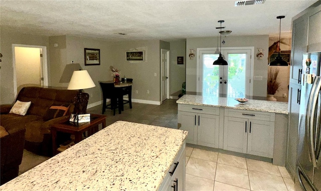 kitchen featuring stainless steel refrigerator, light stone countertops, light tile patterned flooring, and pendant lighting