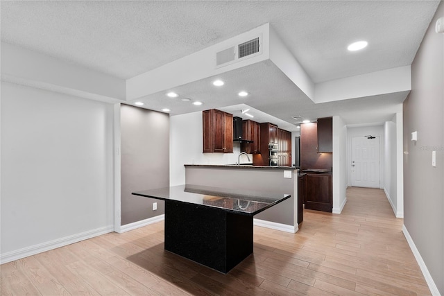 kitchen with light hardwood / wood-style floors, wall chimney exhaust hood, a textured ceiling, a kitchen bar, and a center island