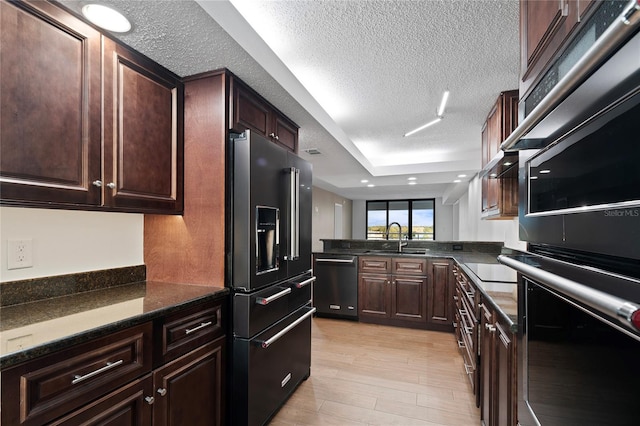 kitchen with sink, a textured ceiling, appliances with stainless steel finishes, dark stone countertops, and light wood-type flooring