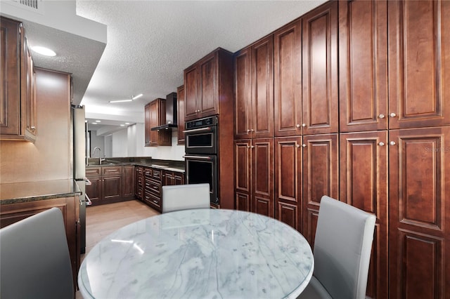 kitchen featuring a textured ceiling, stainless steel appliances, sink, and wall chimney range hood