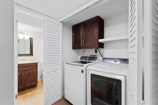 laundry area featuring washing machine and clothes dryer, sink, light hardwood / wood-style flooring, and cabinets