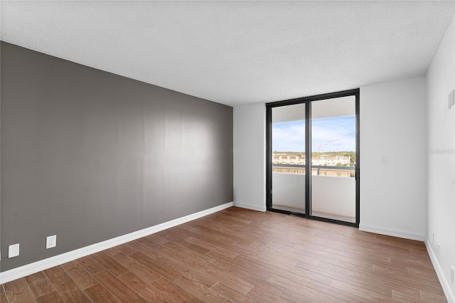 empty room with a textured ceiling, a wall of windows, and light hardwood / wood-style floors