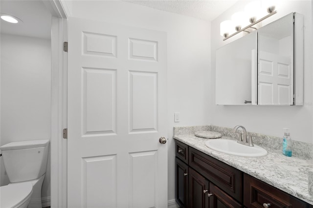 bathroom with a textured ceiling, vanity, and toilet