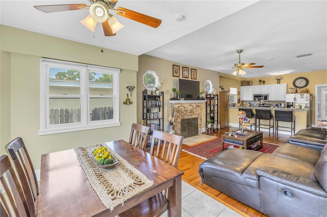 dining room with a fireplace, light hardwood / wood-style floors, and ceiling fan