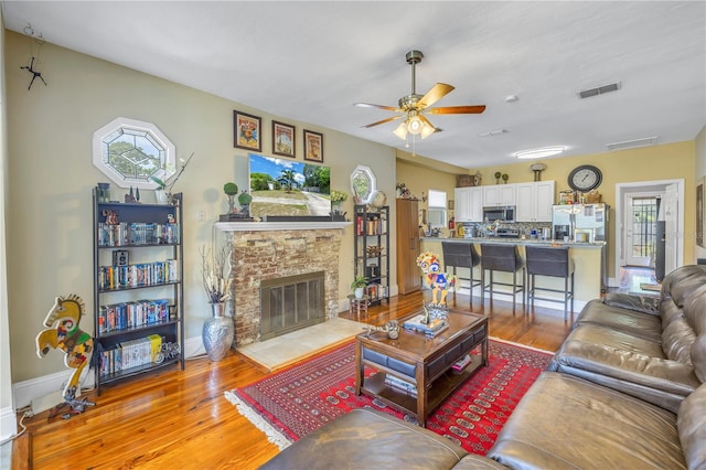 living room with a brick fireplace, hardwood / wood-style floors, and ceiling fan