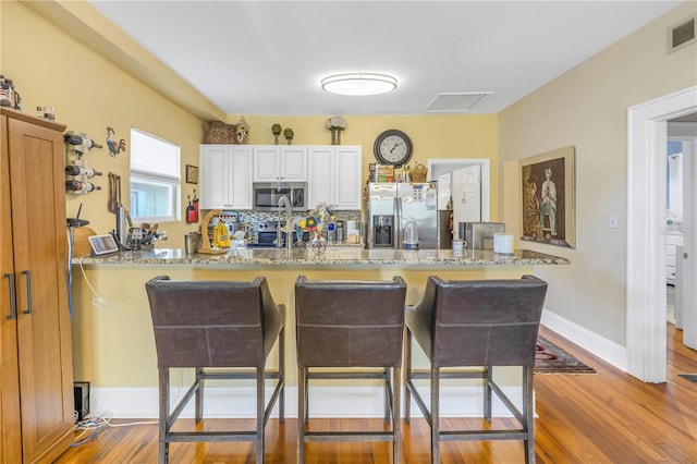 kitchen featuring stainless steel appliances, light stone counters, white cabinets, hardwood / wood-style floors, and kitchen peninsula