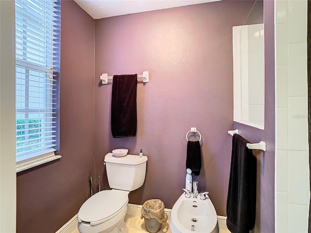 bathroom with baseboards, a bidet, and toilet